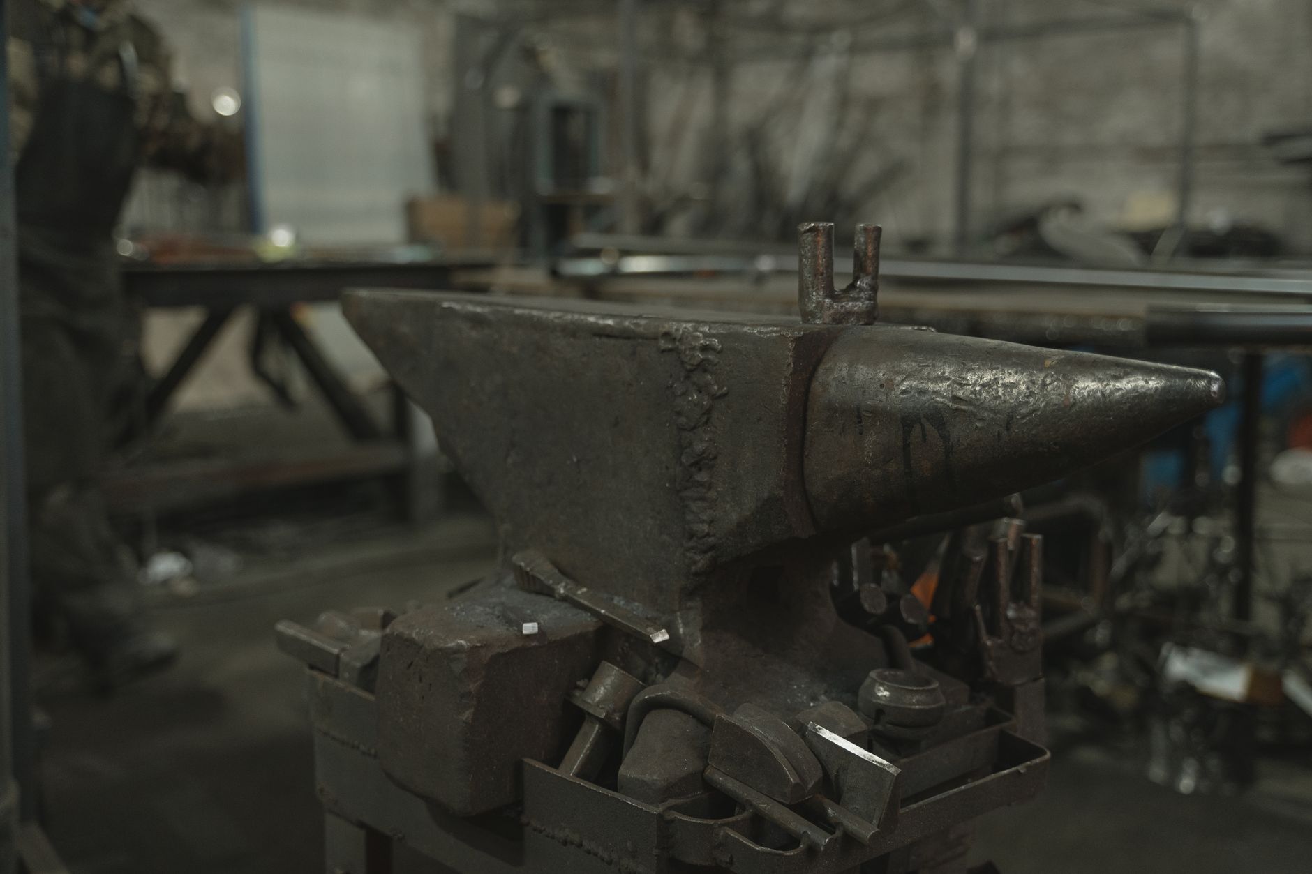 A blacksmith hammers glowing orange steel on an anvil beside an open coal forge