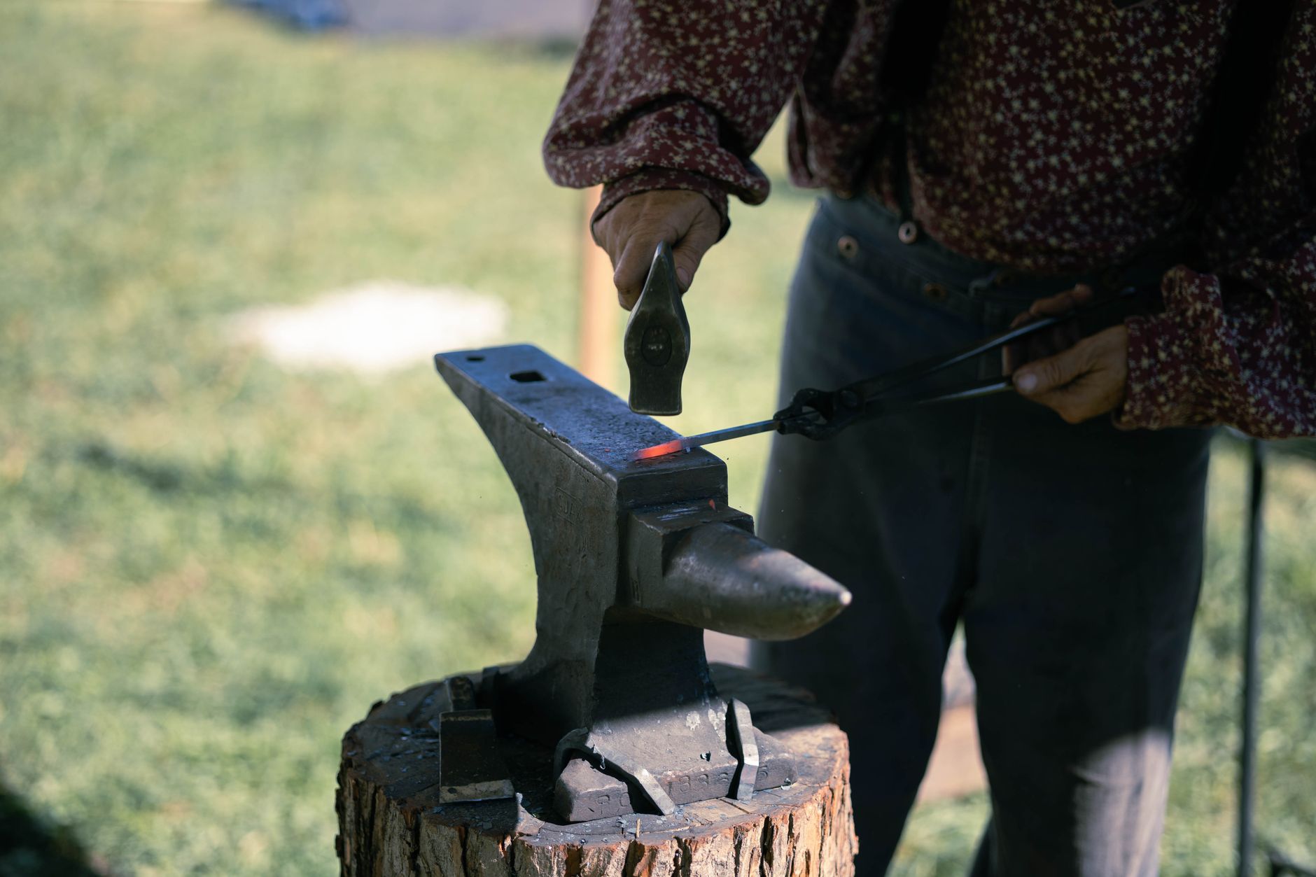 A blacksmith hammers glowing orange metal on an anvil at an outdoor fairground demonstration booth
