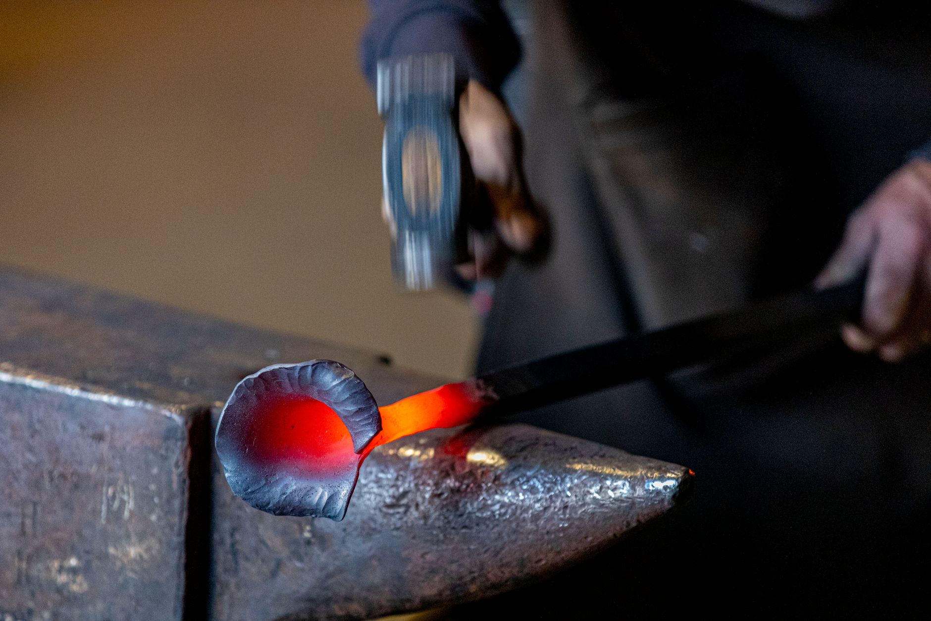 Blacksmith hammering glowing orange metal at an anvil in a community forge workshop